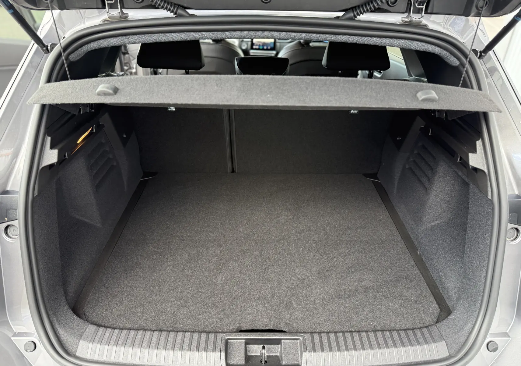 Coffre ouvert vu de l'arrière d'une Renault Symbioz gris cassiopée métal, montrant un espace de chargement vide et propre.