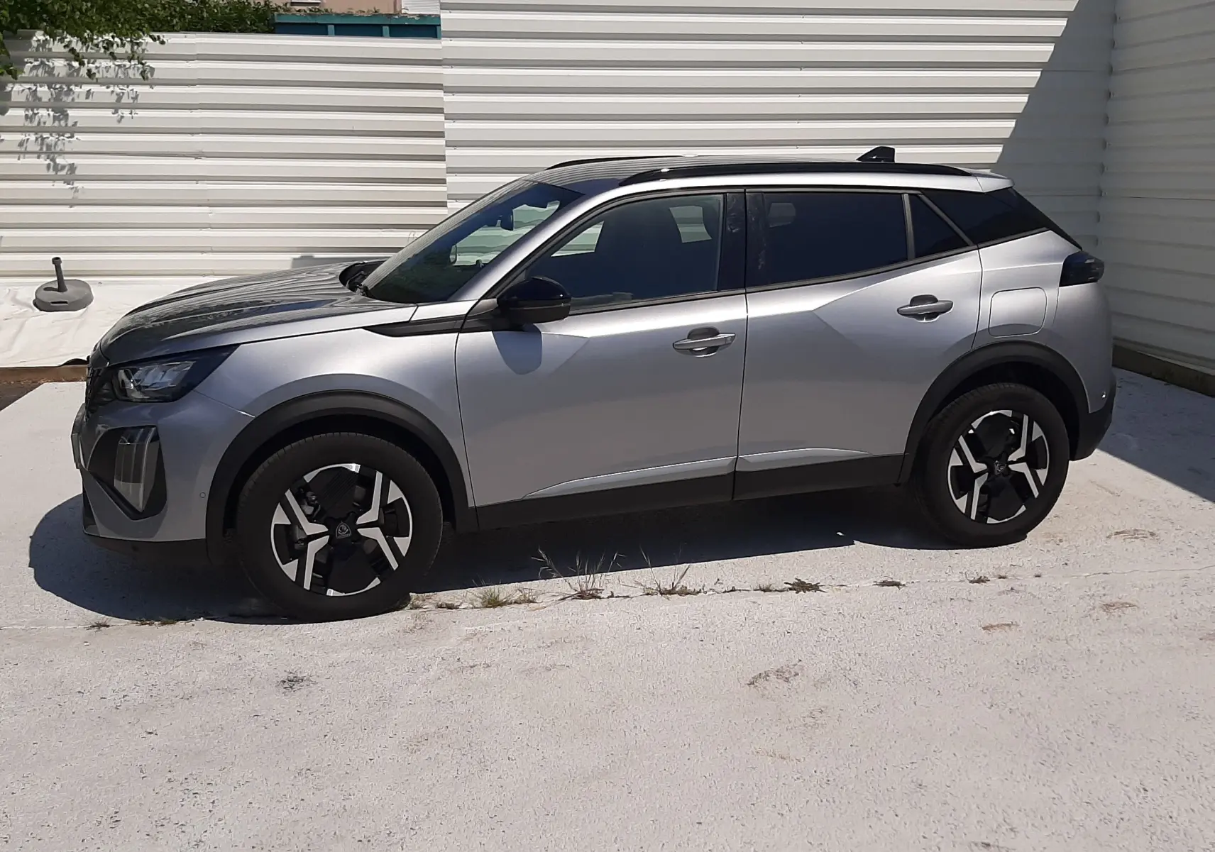 Peugeot 2008 gris Artense vue de profil côté gauche, barres de toit noires et jantes distinctives.