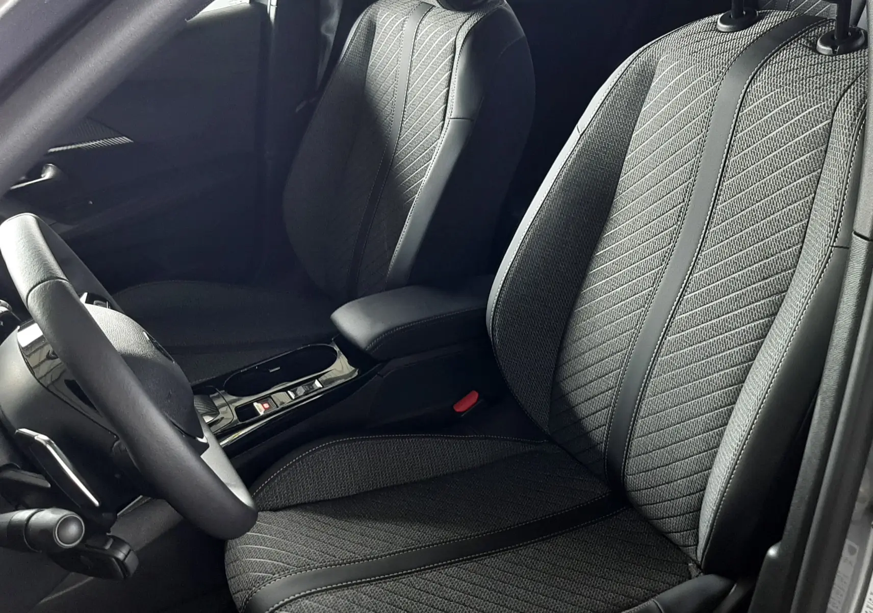 Vue intérieure côté conducteur du Peugeot 2008 gris Artense 2025, sièges tissu noir avec surpiqûres et accoudoir central.
