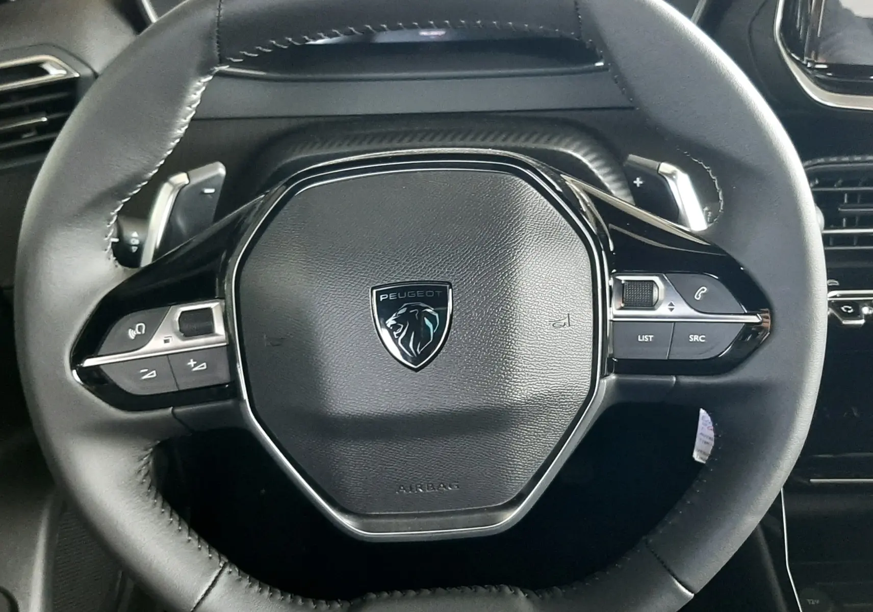 Gros plan sur le volant noir du Peugeot 2008 1.2 Hybrid 145ch Allure, avec commandes intégrées et logo central.