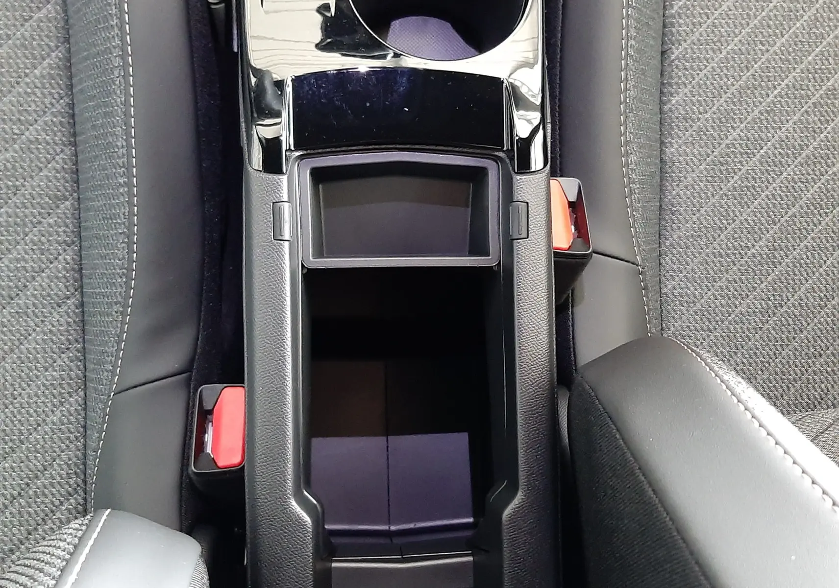 Vue plongeante sur la console centrale noire du Peugeot 2008 1.2 Hybrid 145ch Allure avec porte-gobelets et sièges tissu gris.