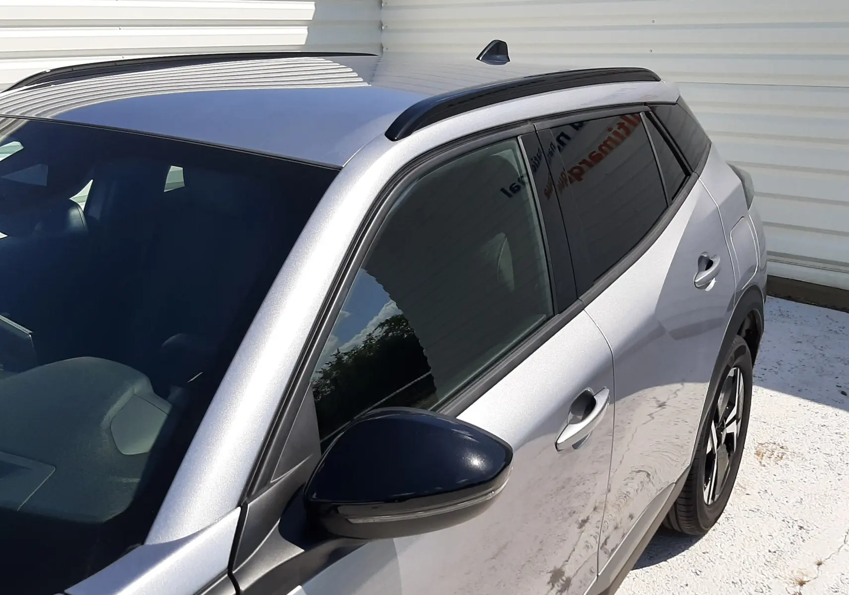 Vue de côté droit avant d’un Peugeot 2008 gris Artense avec barres de toit noires et vitres teintées.