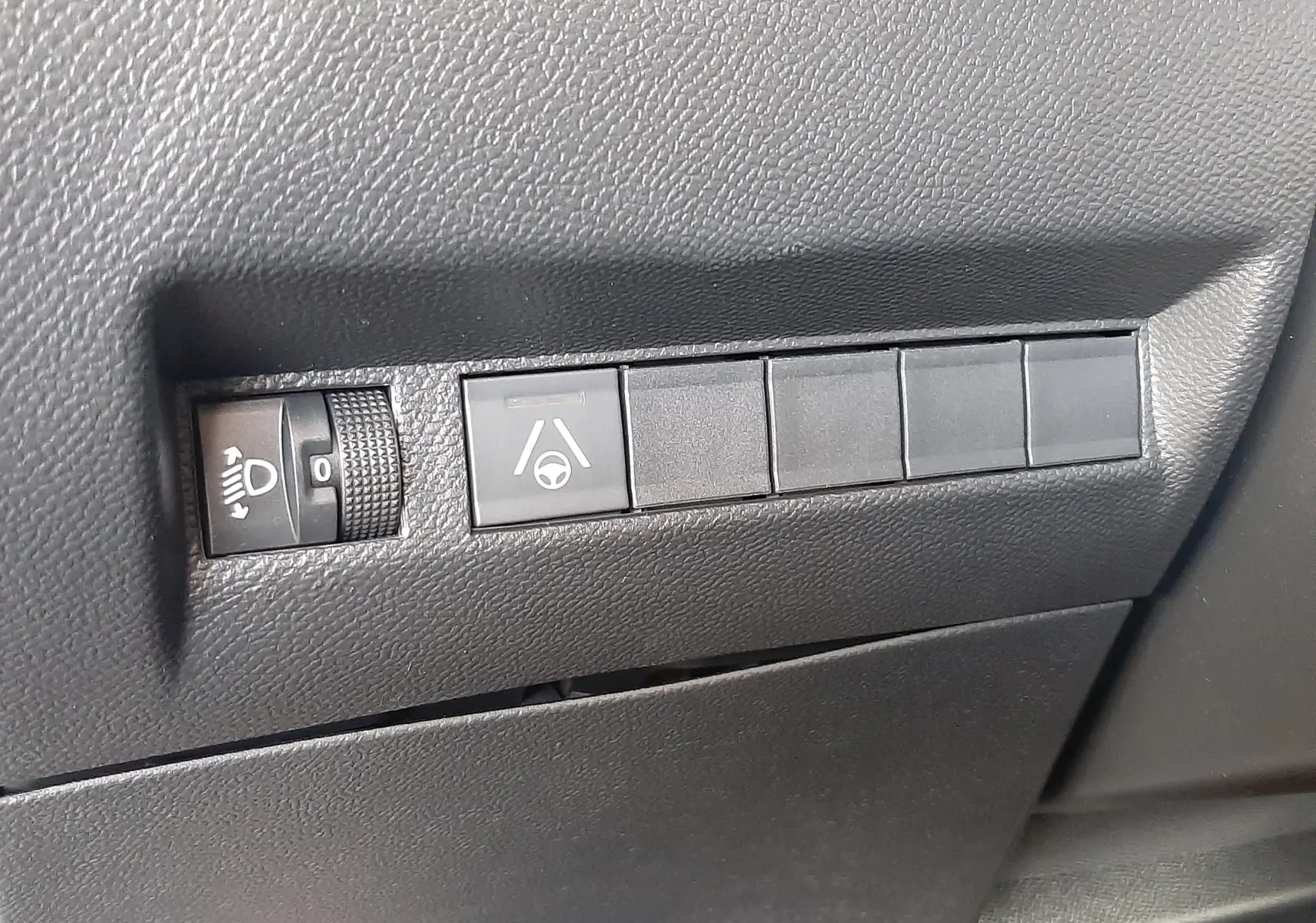 Détail intérieur montrant les commandes de réglage des phares et d'assistance au maintien de voie sur Peugeot 2008 gris Artense.