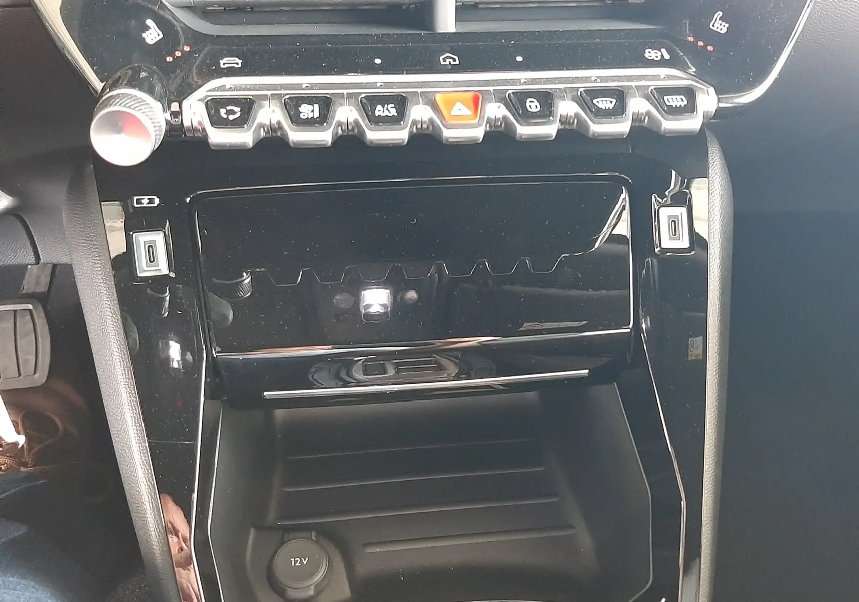 Vue rapprochée de la console centrale noire brillante du Peugeot 2008 1.2 Hybrid 145ch Allure avec commandes tactiles et prise 12V.