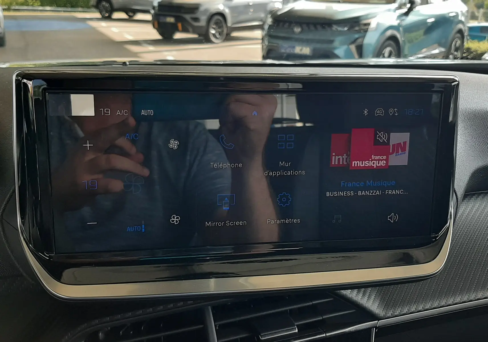 Vue intérieure centrée sur l'écran tactile du tableau de bord du Peugeot 2008, avec reflet d'un véhicule gris Artense à l'extérieur.