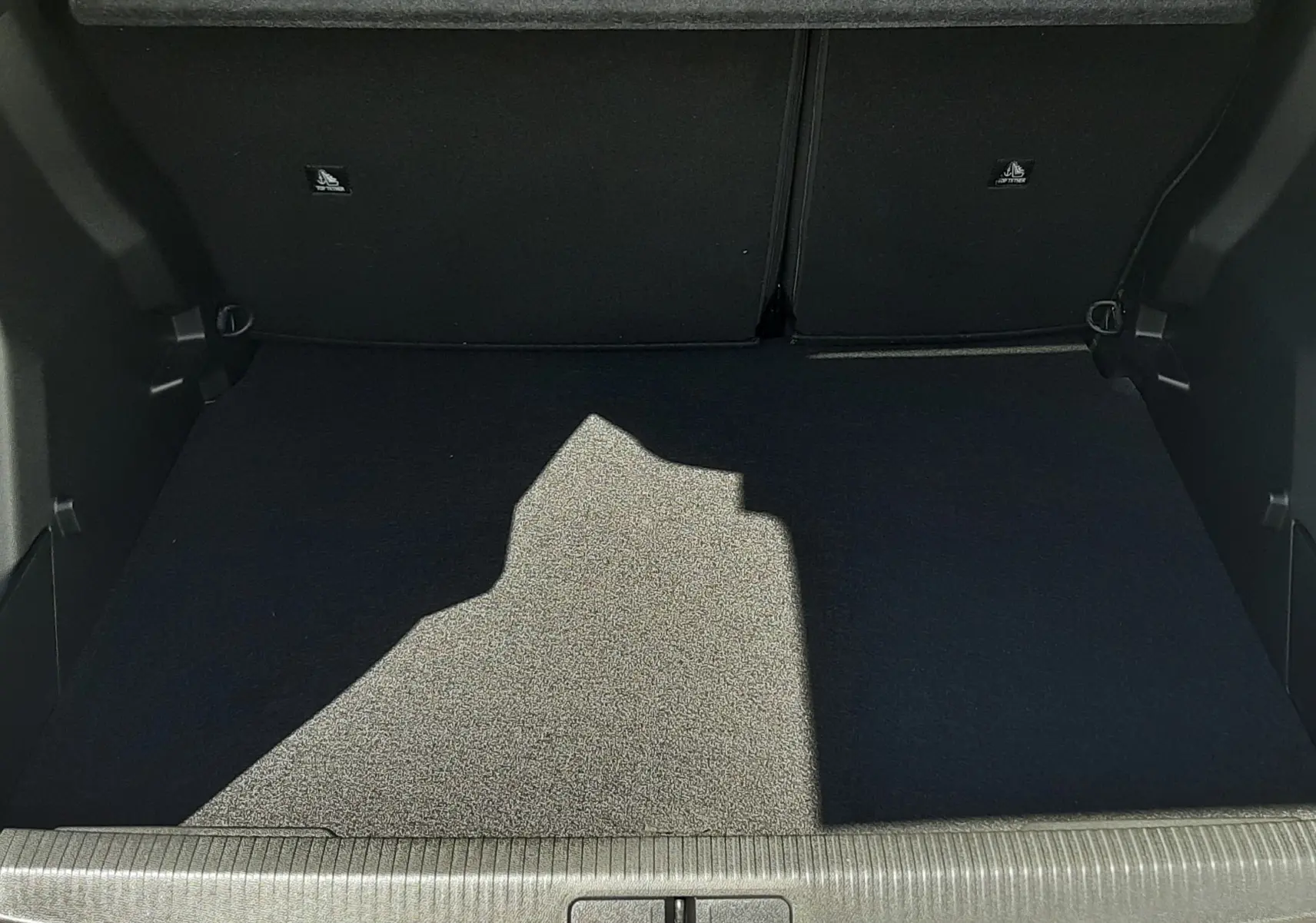 Coffre ouvert vu de l'arrière d'un Peugeot 2008 gris Artense, avec tapis de coffre noir et barres de toit noires visibles.