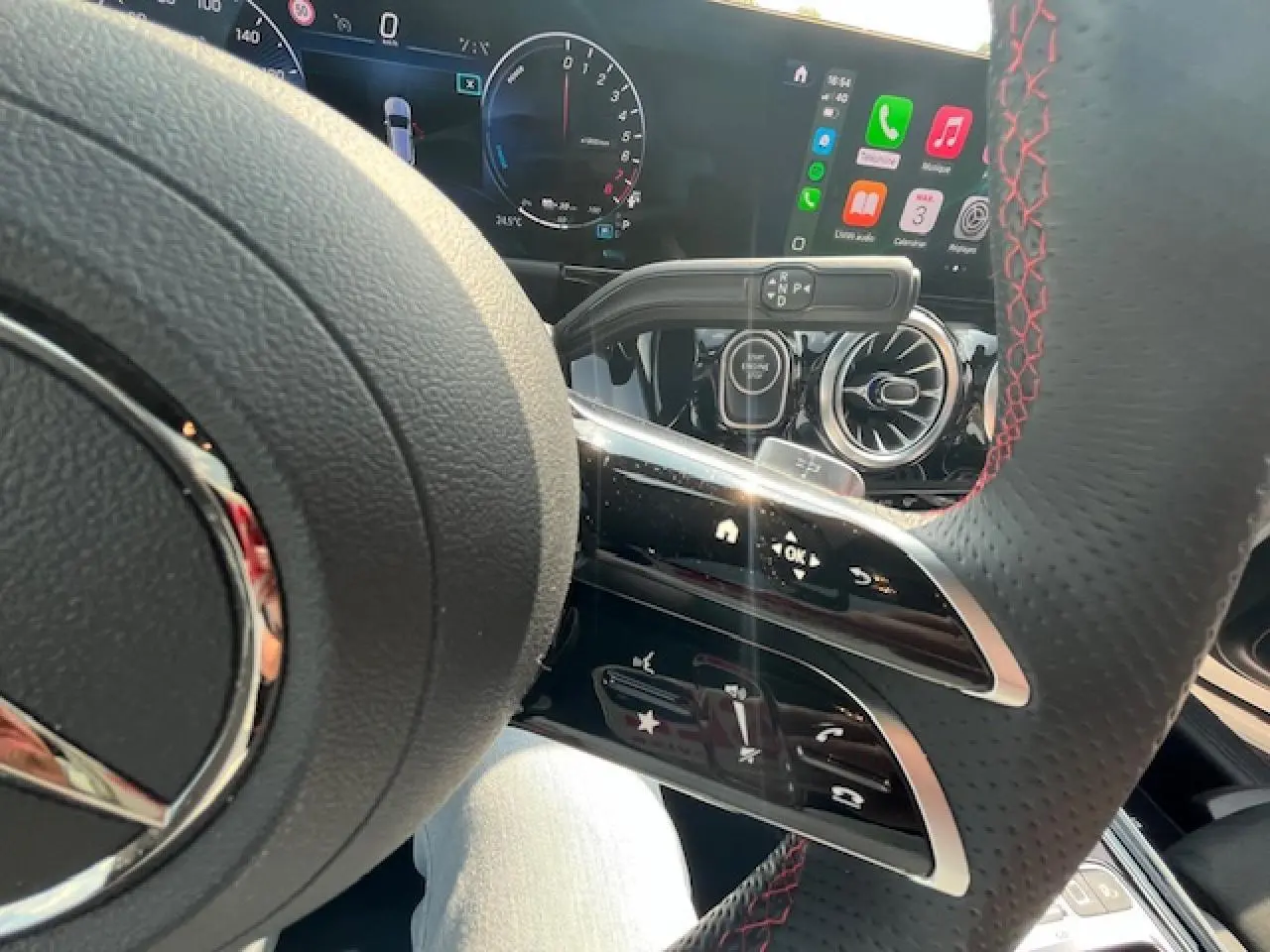 Gros plan sur le volant AMG avec coutures rouges et tableau de bord numérique du Mercedes GLA 250 e blanc 2024 hybride.