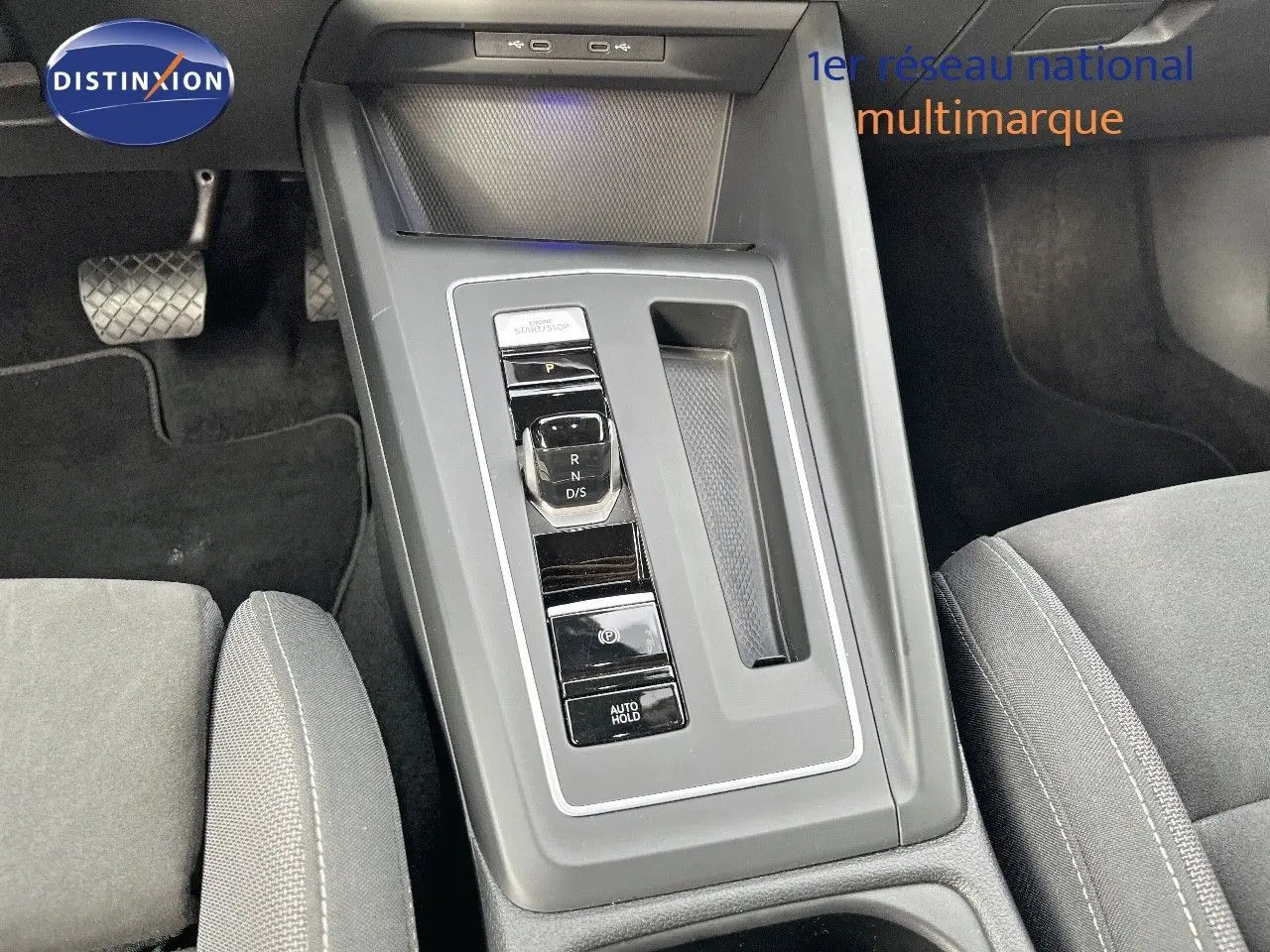 Vue rapprochée de la console centrale grise avec levier de vitesse automatique et sièges tissu gris d'une Volkswagen Golf jaune.