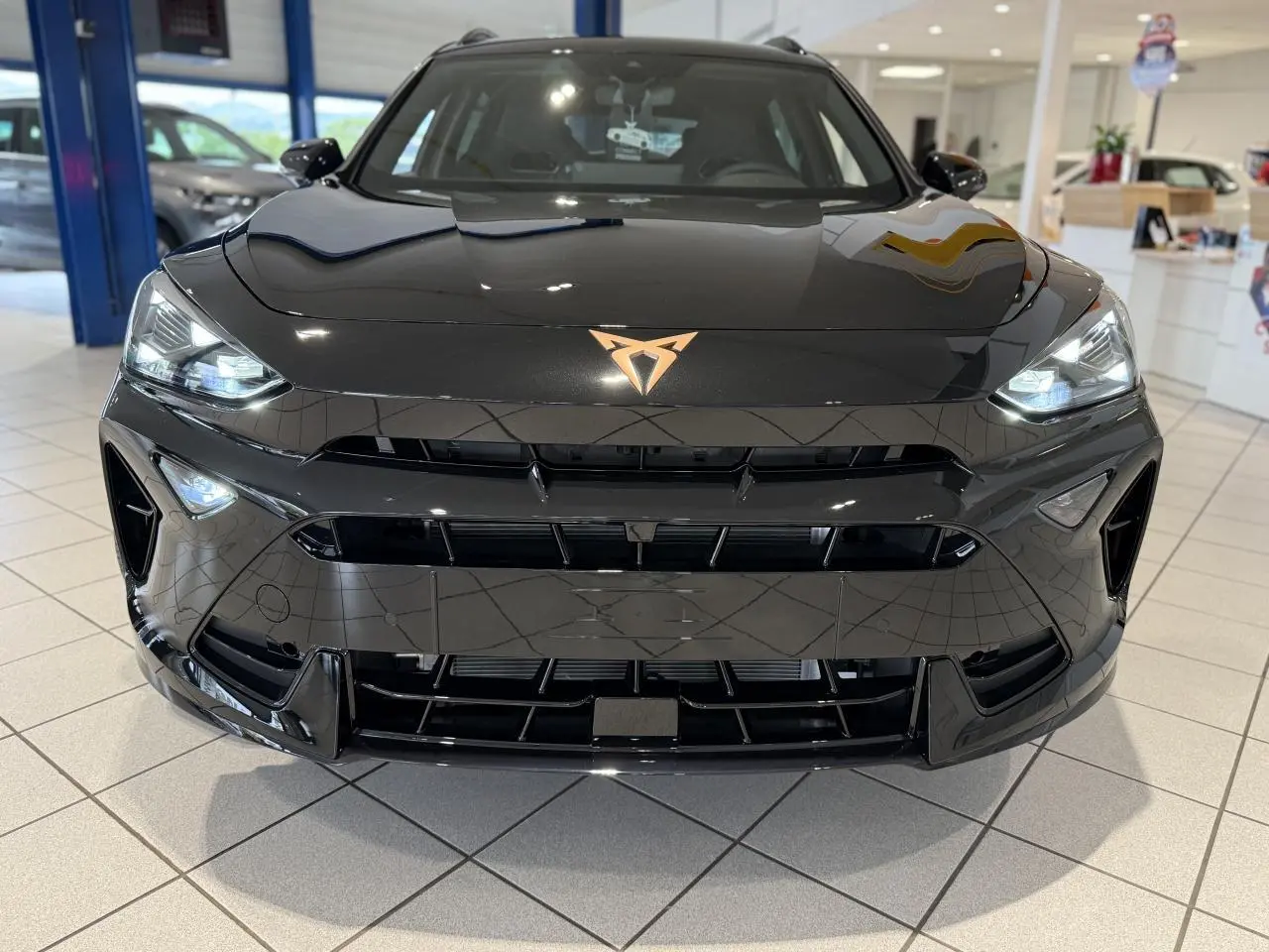 Vue avant rapprochée du CUPRA Formentor noir Night avec logo cuivré et phares Full LED allumés en showroom.