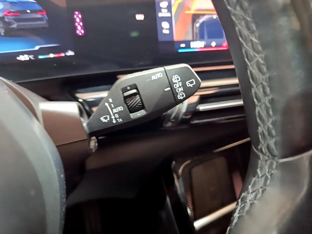 Gros plan sur la commande d’essuie-glace à gauche du volant cuir noir dans l’habitacle d’un BMW X1 noir 2023.