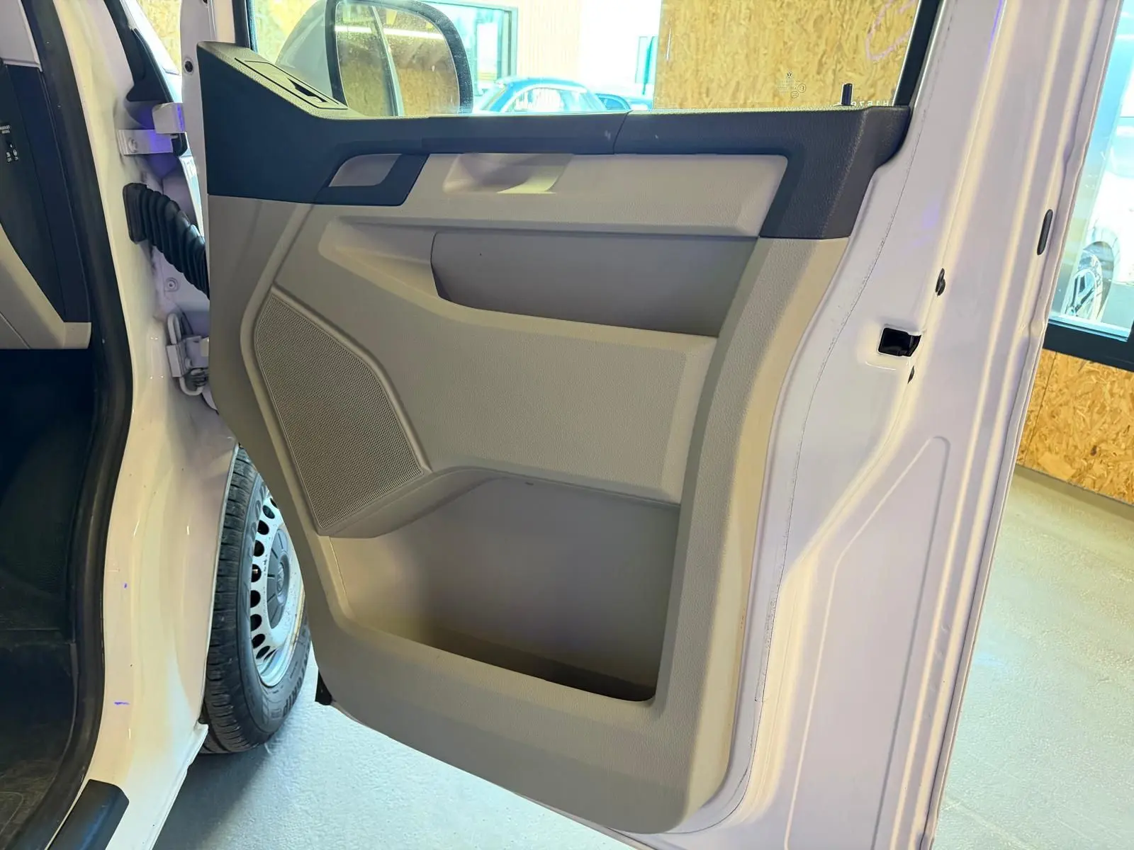 Vue rapprochée de la porte avant gauche blanche du Volkswagen Transporter 2019, avec panneau intérieur beige et noir.