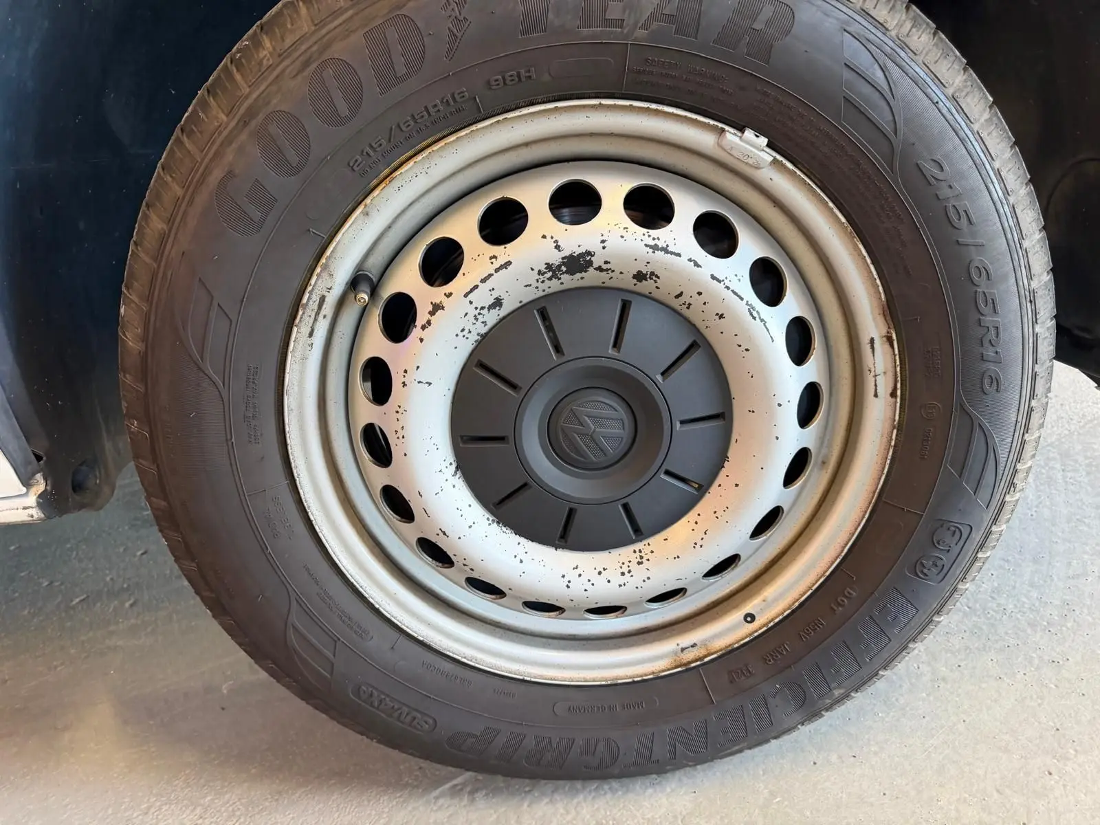 Gros plan sur la roue avant droite d’un Volkswagen Transporter blanc, jante acier avec logo VW au centre.