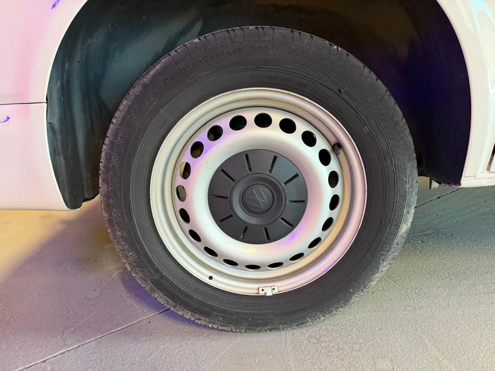 Gros plan sur la roue avant gauche du Volkswagen Transporter blanc, mettant en valeur la jante acier avec logo central.