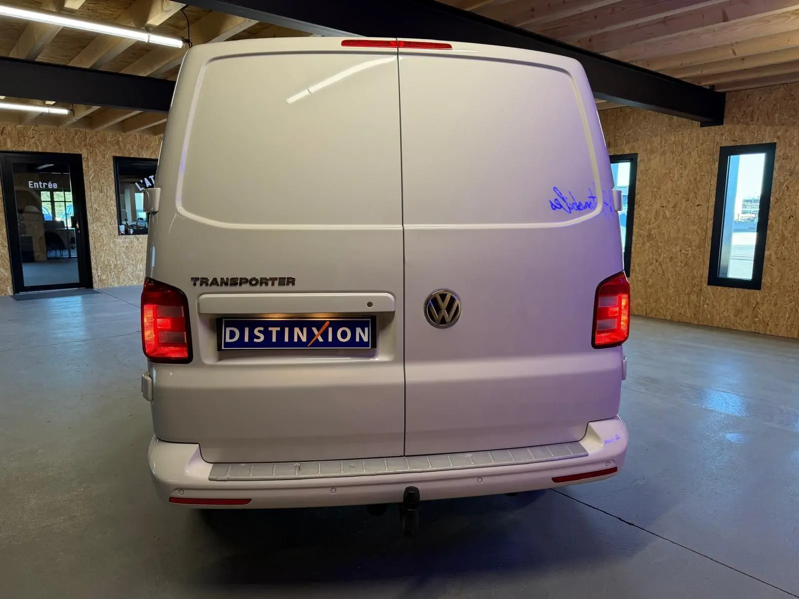 Vue arrière d'un Volkswagen Transporter blanc 2019 avec portes battantes et plaque Distinxion visible en intérieur.