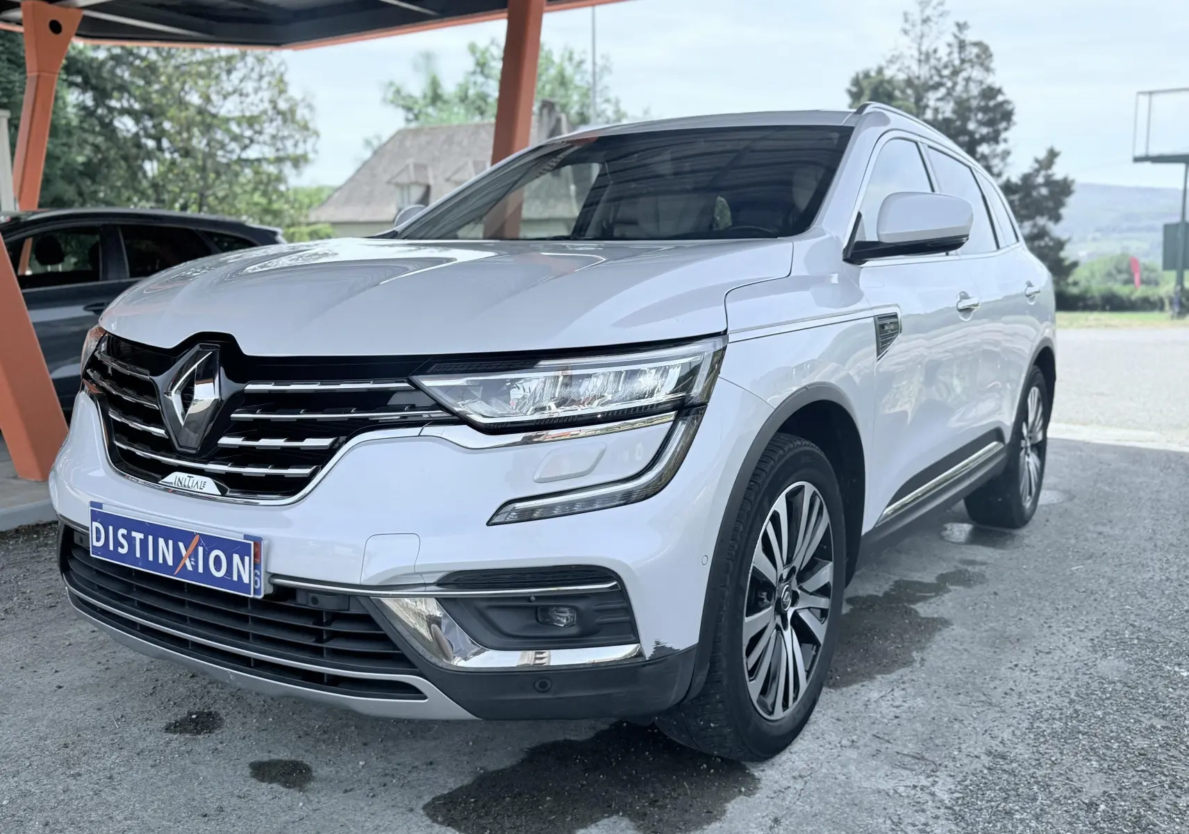 Renault Koleos blanc en 3/4 avant droit sous abri, avec calandre chromée et jantes alliage distinctives.