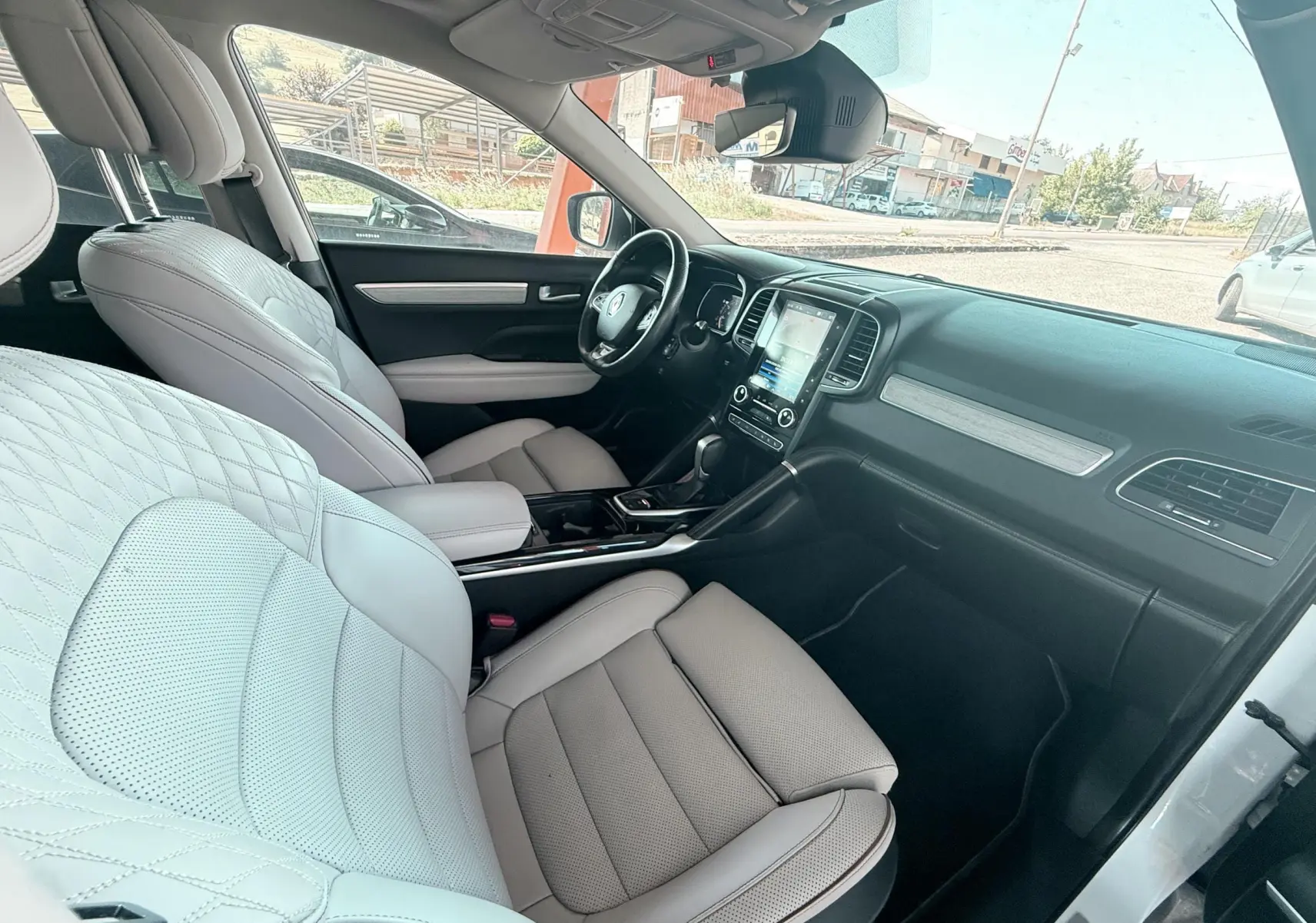 Vue intérieure côté conducteur du Renault Koleos blanc, mettant en valeur les sièges cuir beige et la console centrale moderne.
