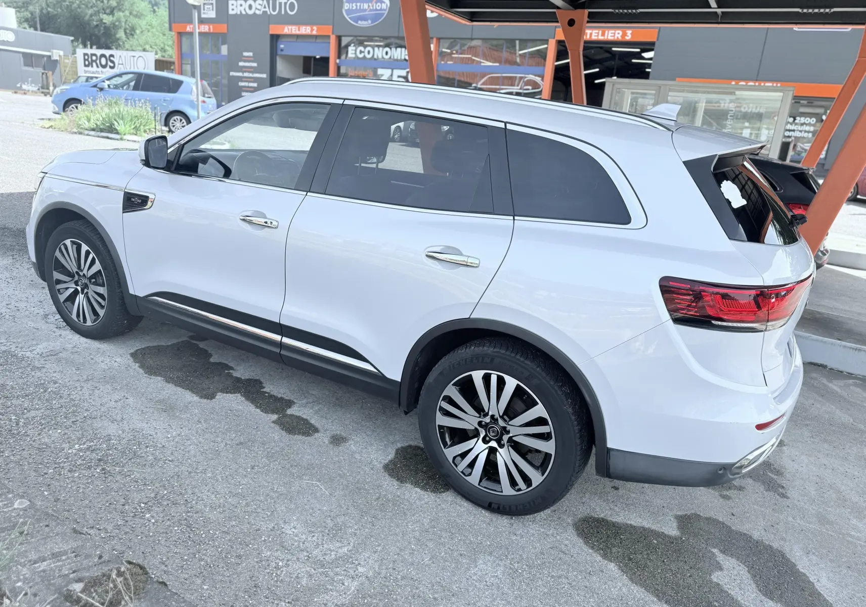 Vue 3/4 arrière droite d'un Renault Koleos blanc garé sous un abri avec jantes alliage et vitres teintées.