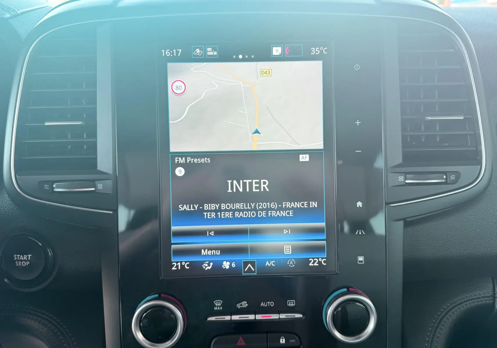 Vue rapprochée de l’écran tactile central du tableau de bord du Renault Koleos blanc, affichant la navigation et la radio.