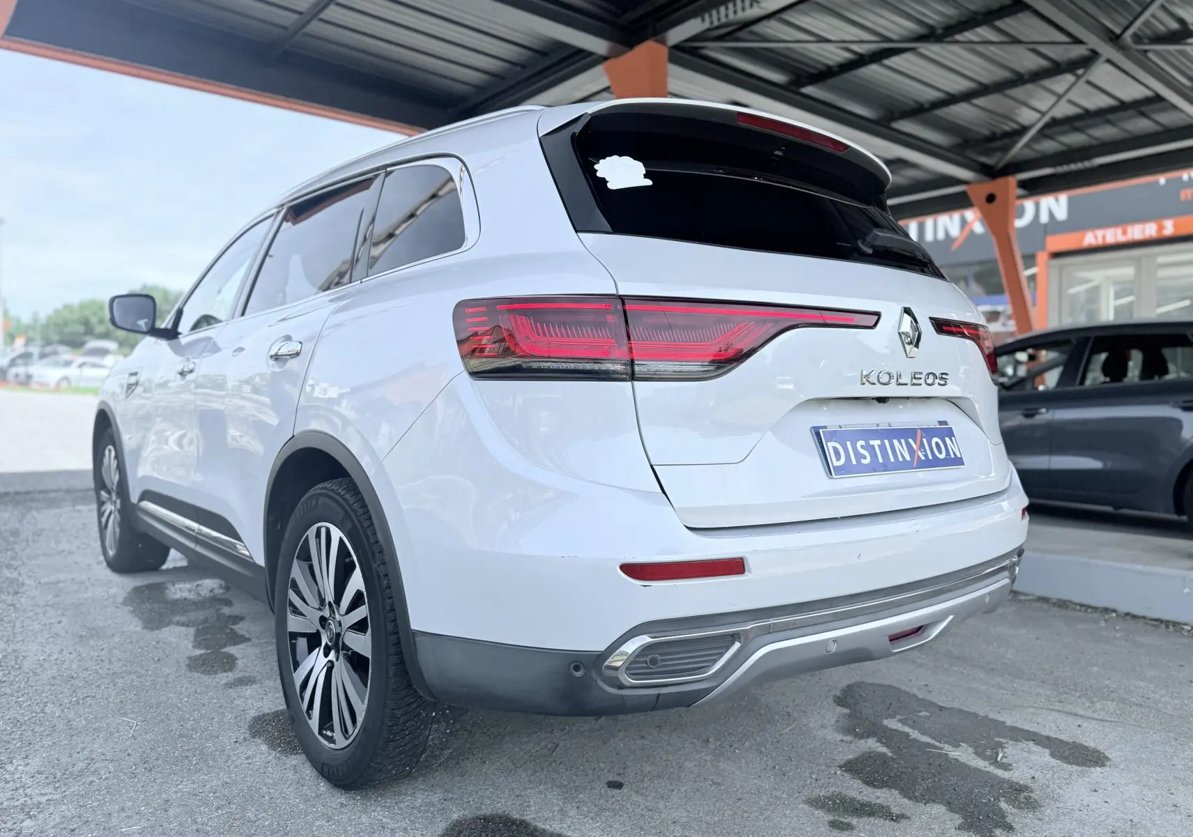 Vue 3/4 arrière droite d’un Renault Koleos blanc garé sous un abri avec feux arrière allongés et jantes alliage.