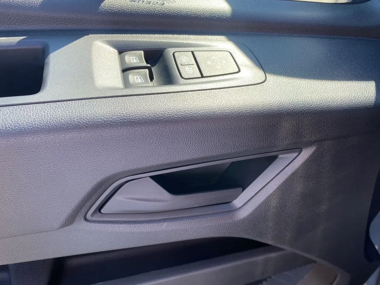 Poignée intérieure côté gauche de la porte avant du Renault Master gris urbain, avec commandes des vitres et rétroviseurs.
