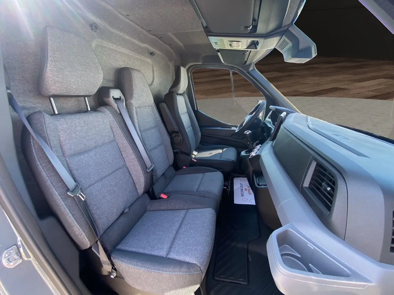 Vue intérieure côté passager du Renault Master 2025, sièges tissu gris chiné avec surpiqûres bleues et tableau de bord gris.