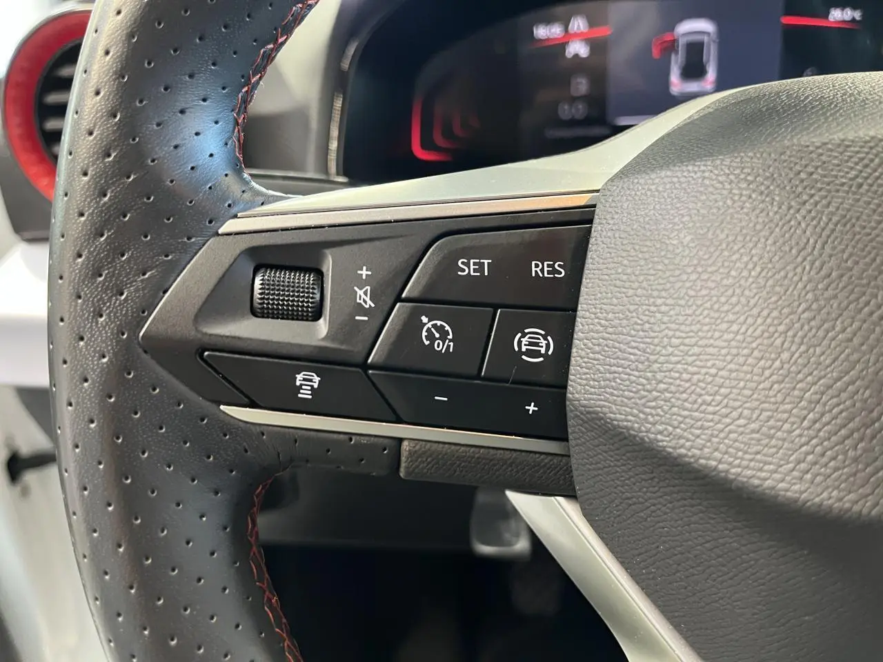 Gros plan sur le volant cuir perforé côté gauche du SEAT Arona blanc Nevada 2024 avec commandes de régulateur et aide à la conduite.