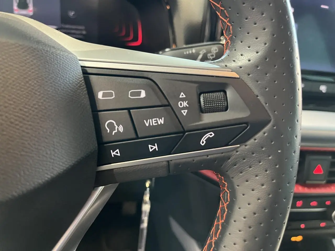 Gros plan sur le volant sport cuir noir avec surpiqûres rouges du SEAT Arona 2024, boutons multifonctions visibles.