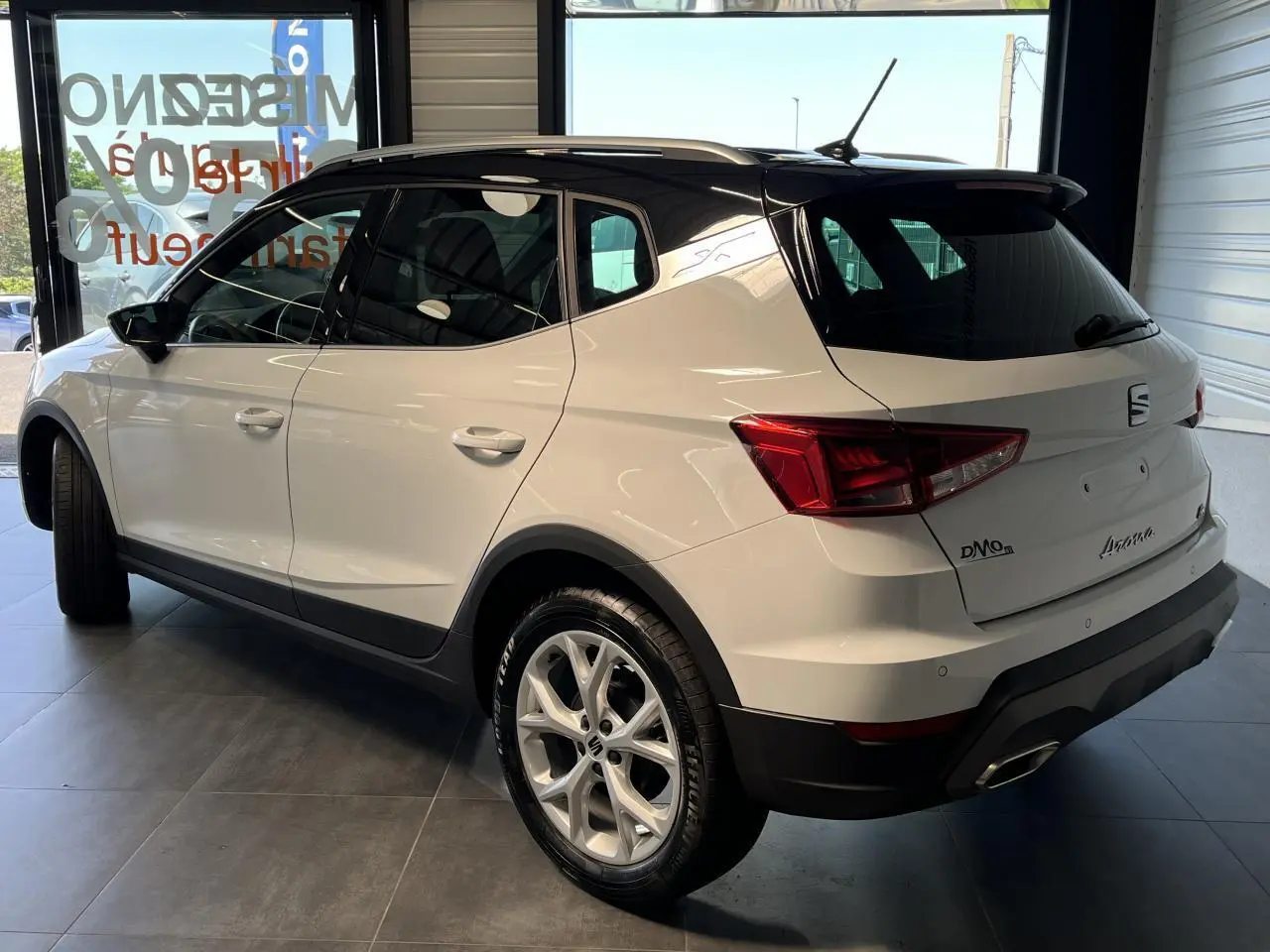 SEAT Arona blanc Nevada vu en 3/4 arrière droit, toit noir et jantes alliage 16 pouces en showroom.