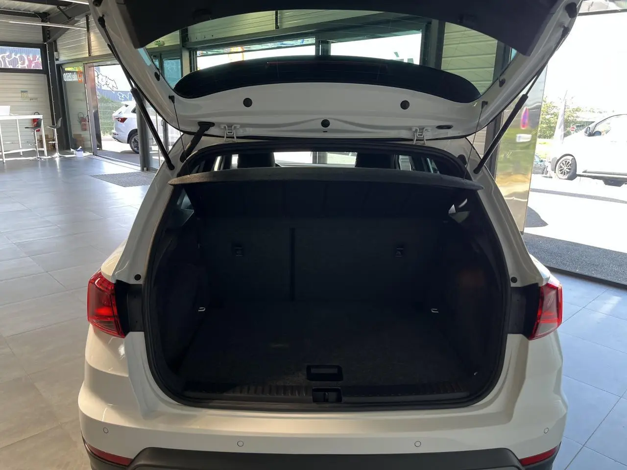 Coffre ouvert vu de l'arrière d'un SEAT ARONA blanc Nevada 2024, intérieur spacieux et tapis noir.