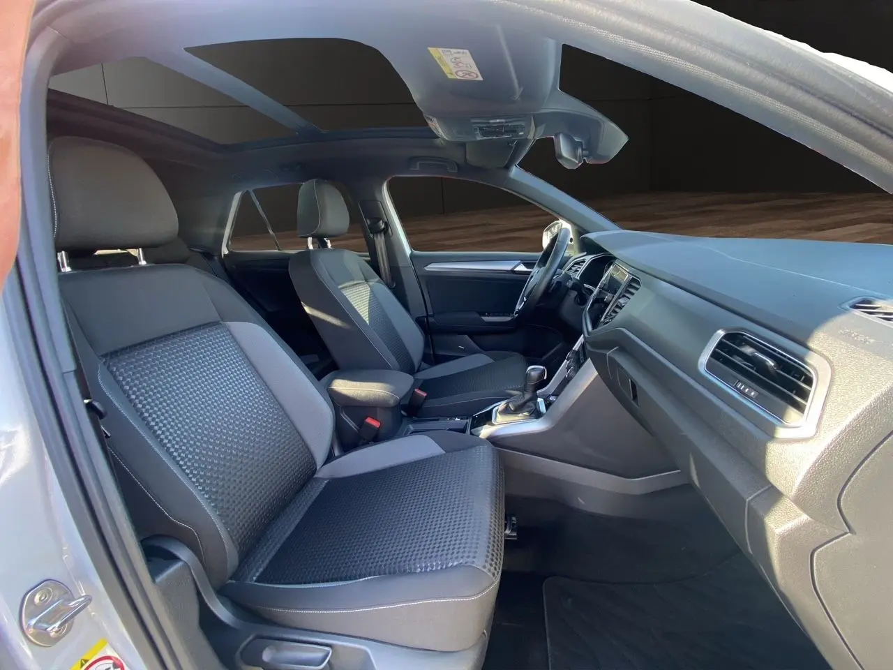 Intérieur noir du Volkswagen T-Roc 2021 vu côté gauche, avec toit ouvrant panoramique et sièges avant en tissu.