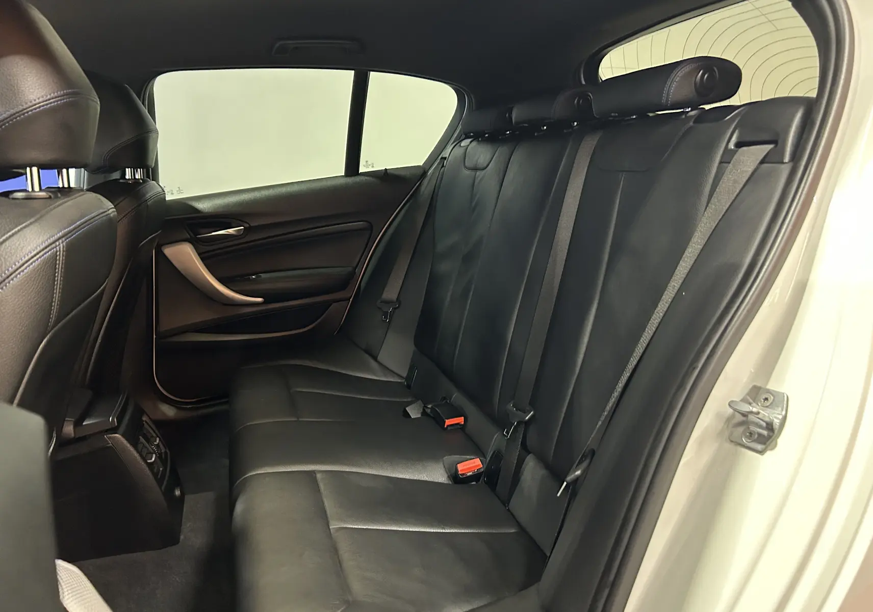 Vue latérale droite de l'intérieur arrière d'une BMW Série 1 blanche, sièges en cuir noir avec ceintures de sécurité visibles.
