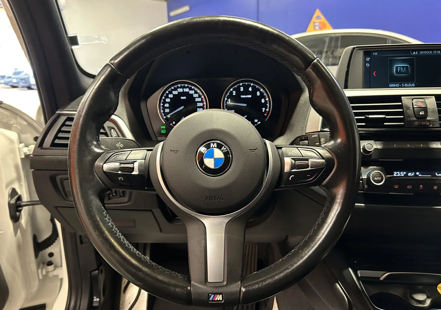 Vue centrée sur le volant cuir M Sport de la BMW Série 1 blanche, avec tableau de bord et écran multimédia visibles.