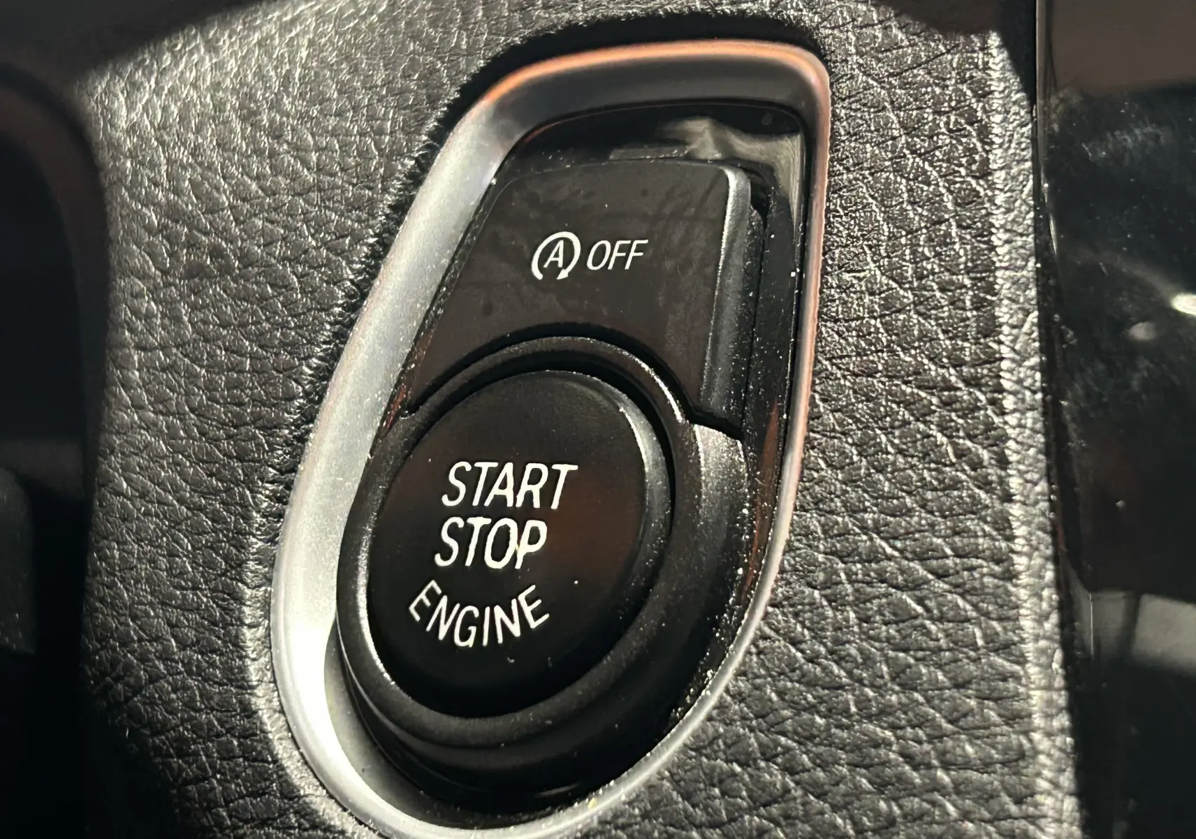 Gros plan sur le bouton Start Stop Engine et la commande Auto Start/Stop désactivée dans l'habitacle d'une BMW Série 1 blanche.