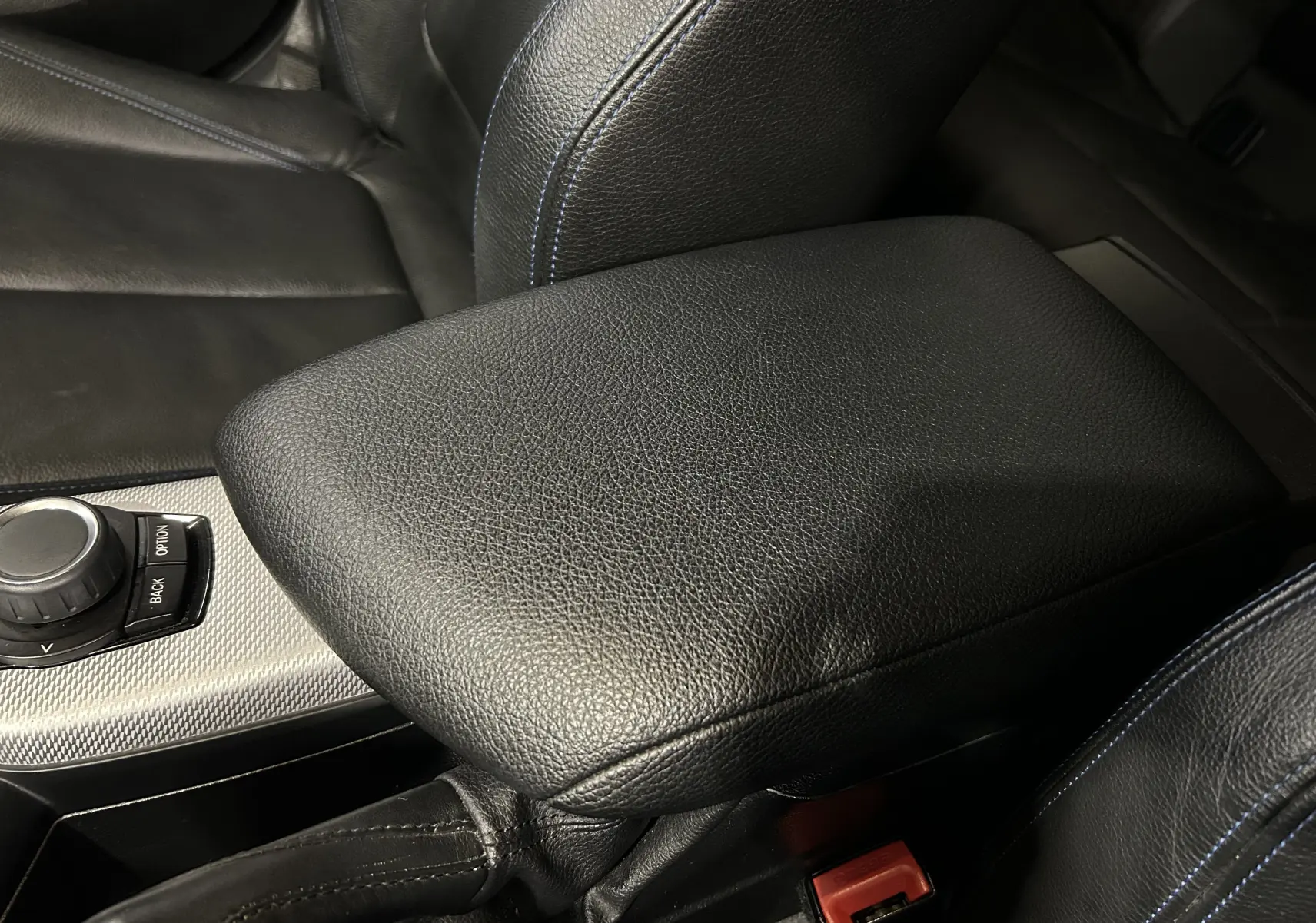 Gros plan sur l'accoudoir central en cuir noir avec surpiqûres bleues dans l'habitacle d'une BMW Série 1 blanche.