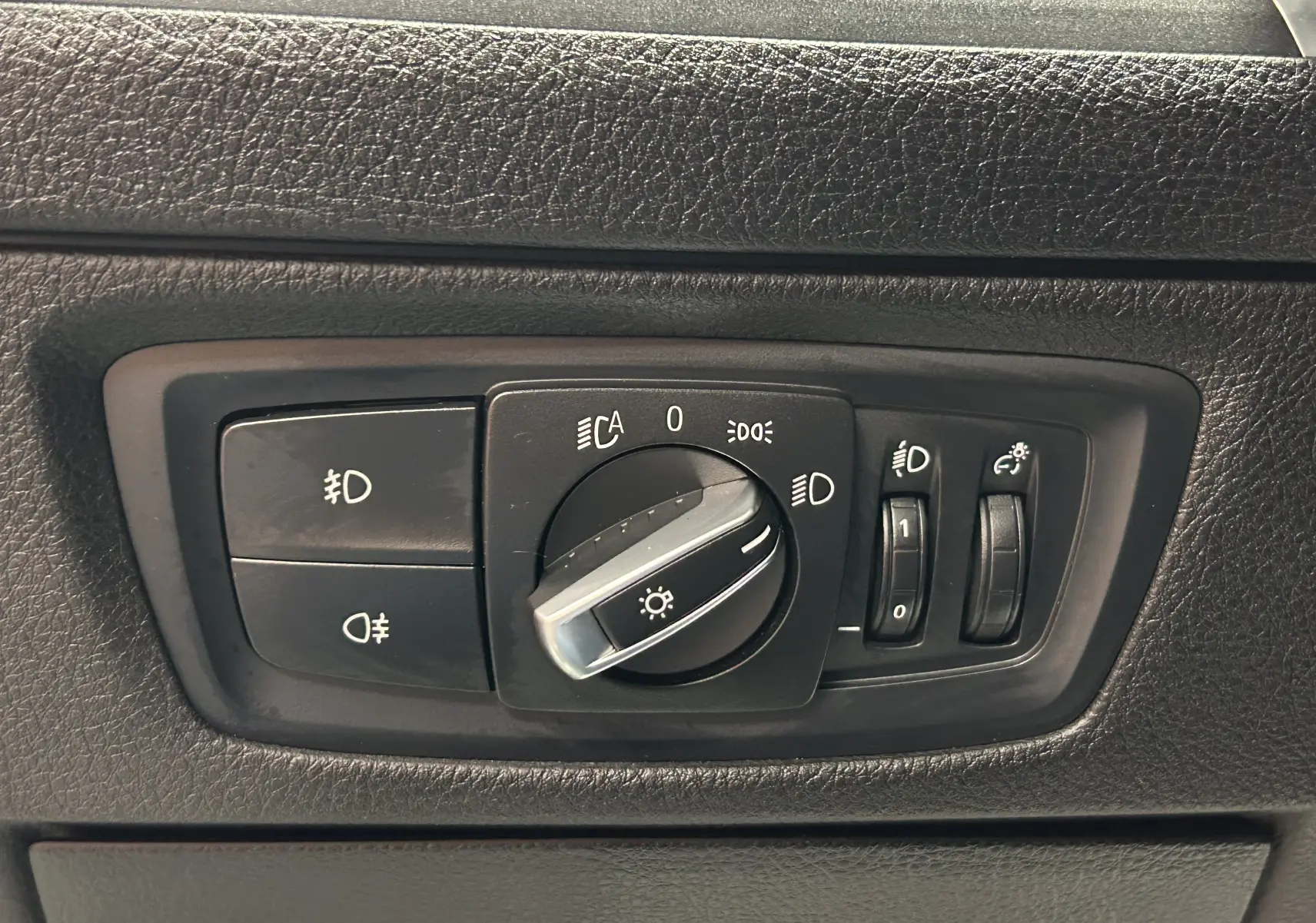 Gros plan sur le panneau de commande des phares d'une BMW Série 1 blanche, version 120iA M Sport de 2019.