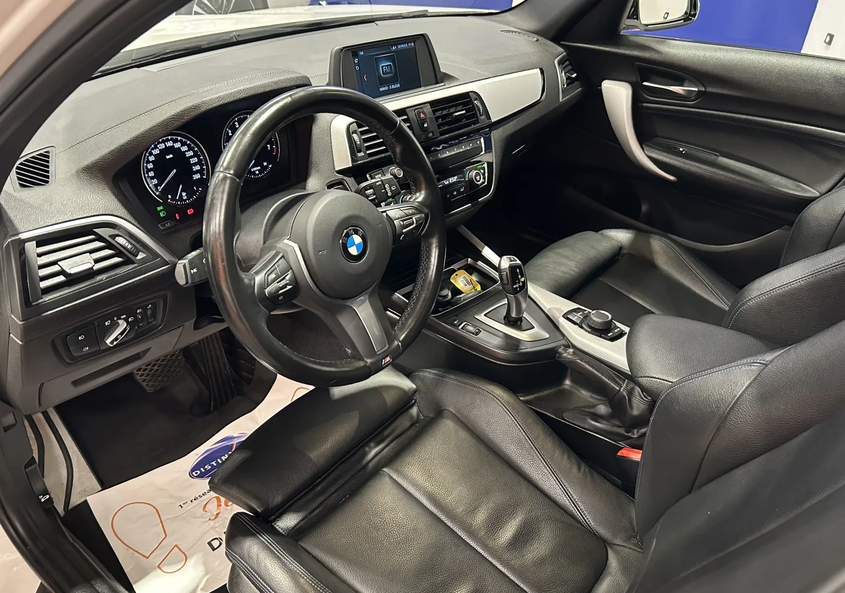 Vue intérieure côté conducteur de la BMW Série 1 120iA M Sport 2019 avec sièges cuir noirs et volant multifonction.