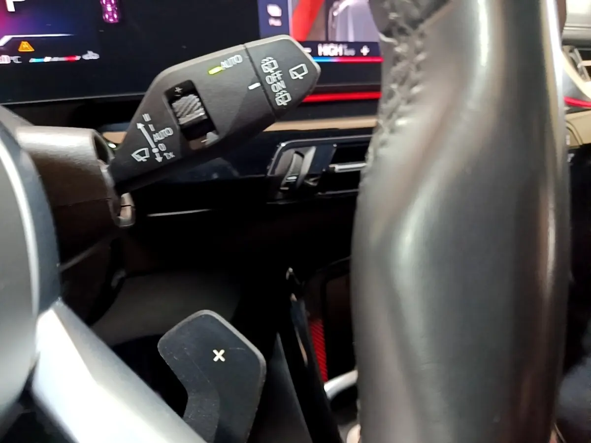 Gros plan sur la commande d'essuie-glace et palette de changement de vitesse derrière le volant cuir d’un BMW X1 gris clair.