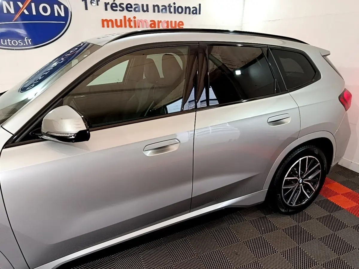 Vue latérale droite d’un BMW X1 gris clair 2023 avec jantes alliage et rétroviseurs électriques noirs.