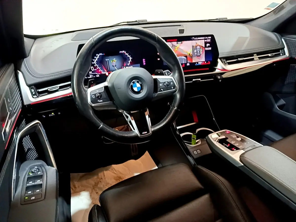 Intérieur BMW X1 xDrive23i M Sport 2023 vu côté conducteur, volant cuir, tableau de bord numérique et écran tactile.