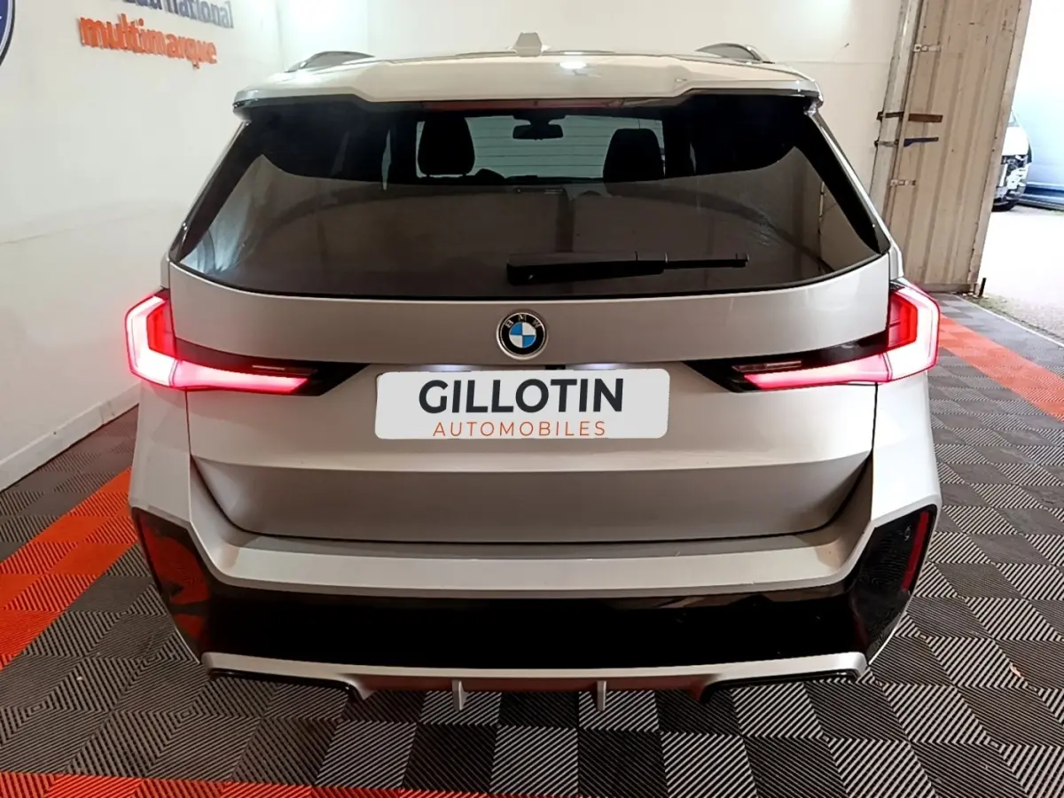 Vue arrière d'un BMW X1 gris clair avec feux LED allumés dans un garage intérieur.