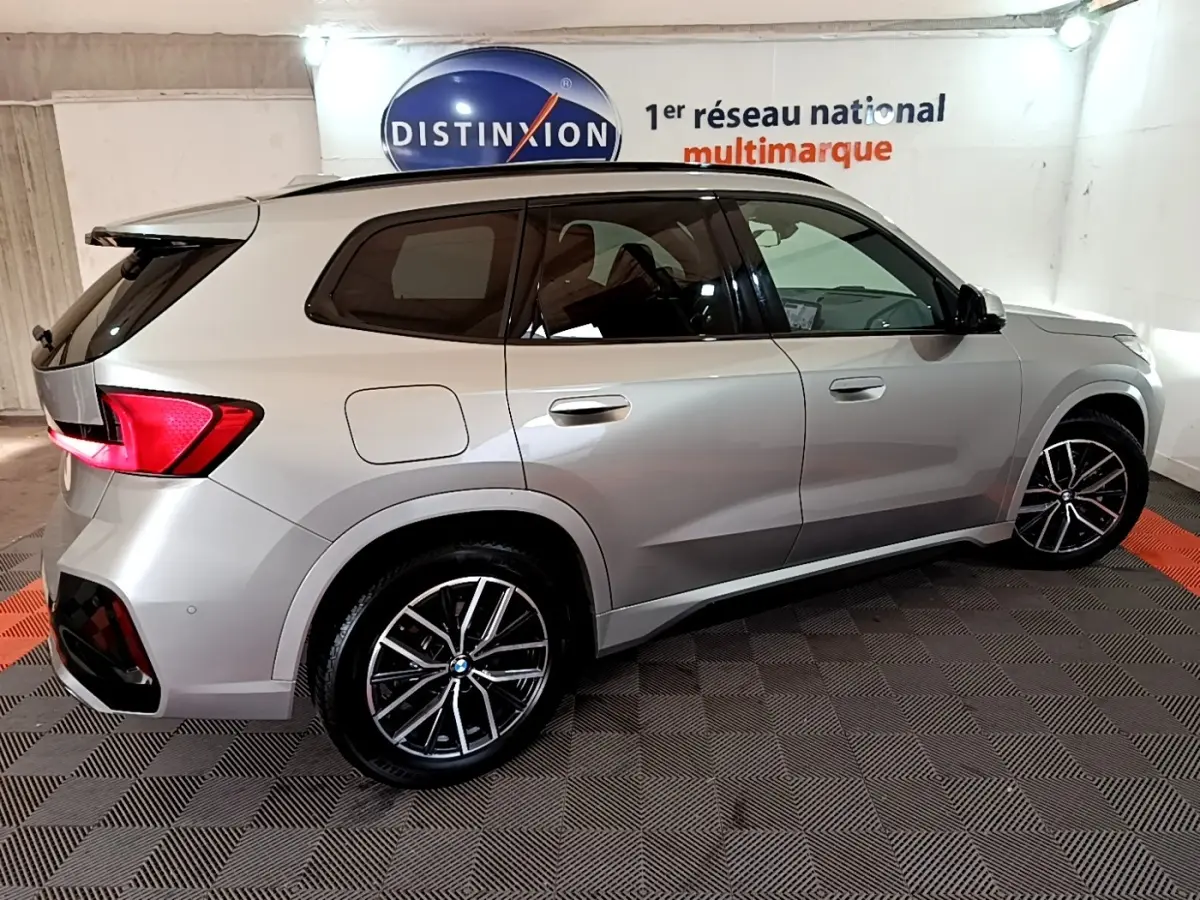 BMW X1 xDrive23i M Sport gris clair vue de profil côté droit dans un showroom avec jantes alliage noires.