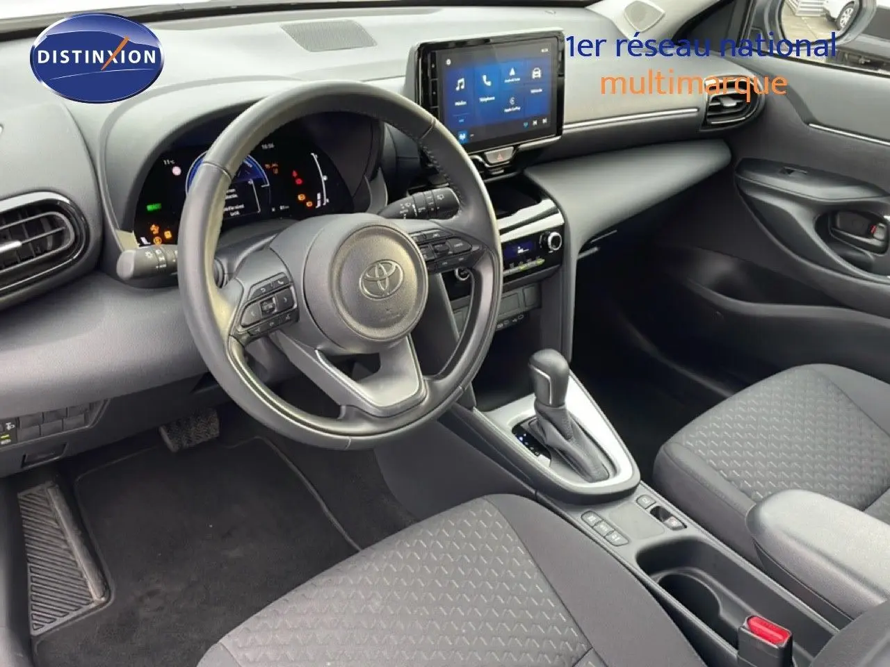 Vue intérieure avant de la Toyota Yaris Cross blanche, montrant le tableau de bord, volant multifonction et écran tactile central.