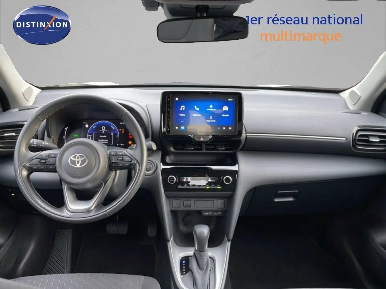Vue frontale de l'intérieur de la Toyota Yaris Cross 2024, tableau de bord noir avec écran tactile central et volant multifonction.