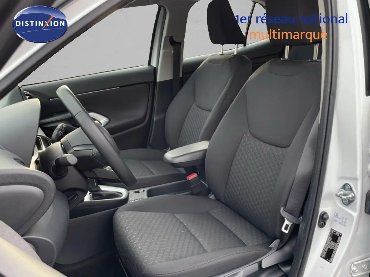 Vue intérieure côté conducteur de la Toyota Yaris Cross 2024 blanche, sièges tissu gris et volant cuir multifonction.