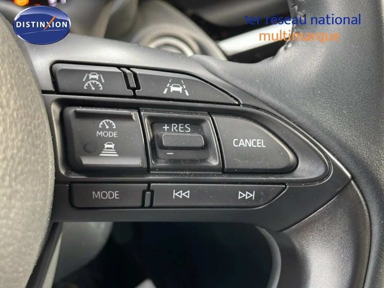 Gros plan sur les commandes au volant noir de la Toyota Yaris Cross 2024, mettant en valeur les boutons de régulateur et multimédia.