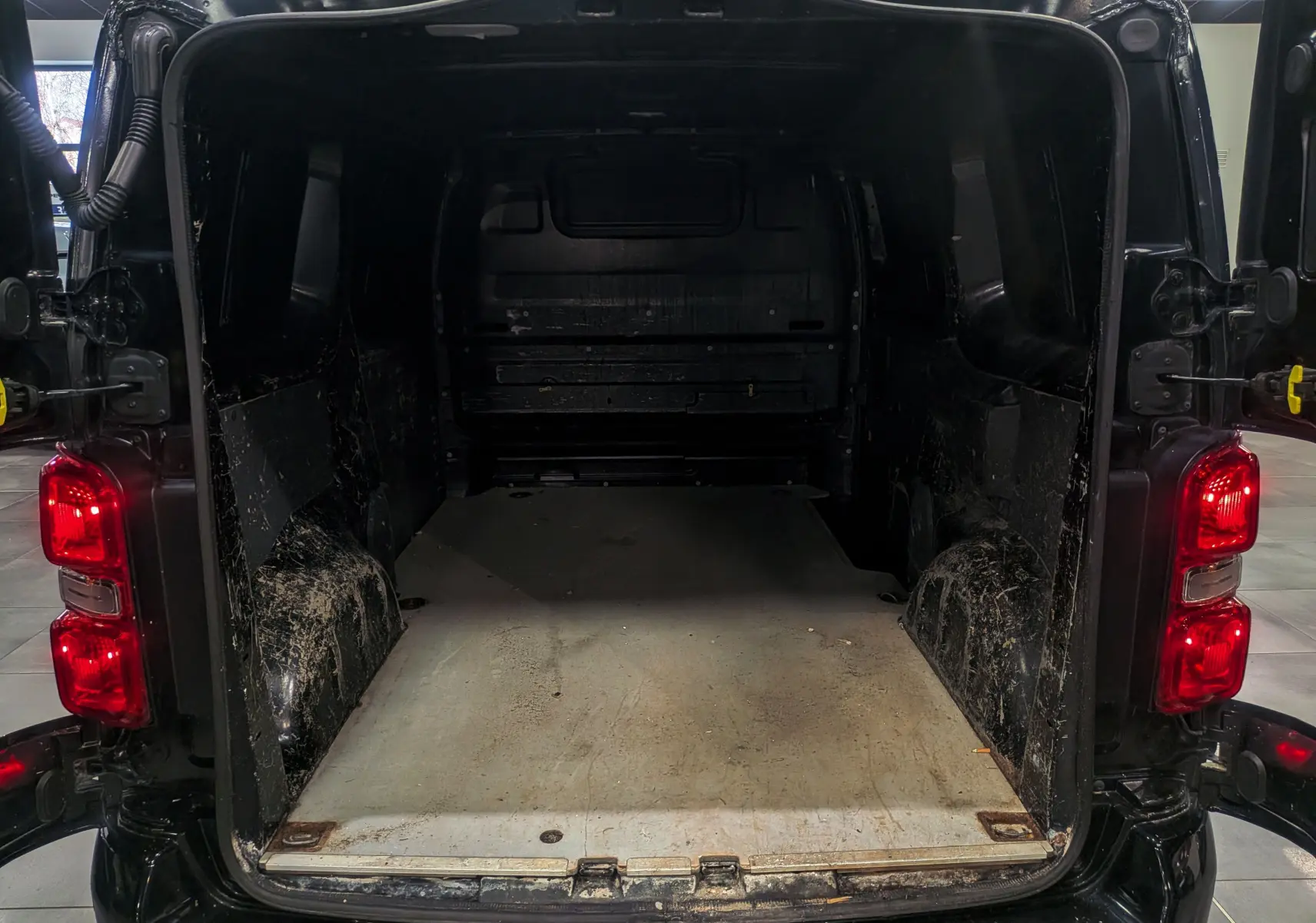 Vue arrière ouverte du Peugeot Expert Fourgon noir Perla, montrant l’espace de chargement vide et les feux arrière allumés.