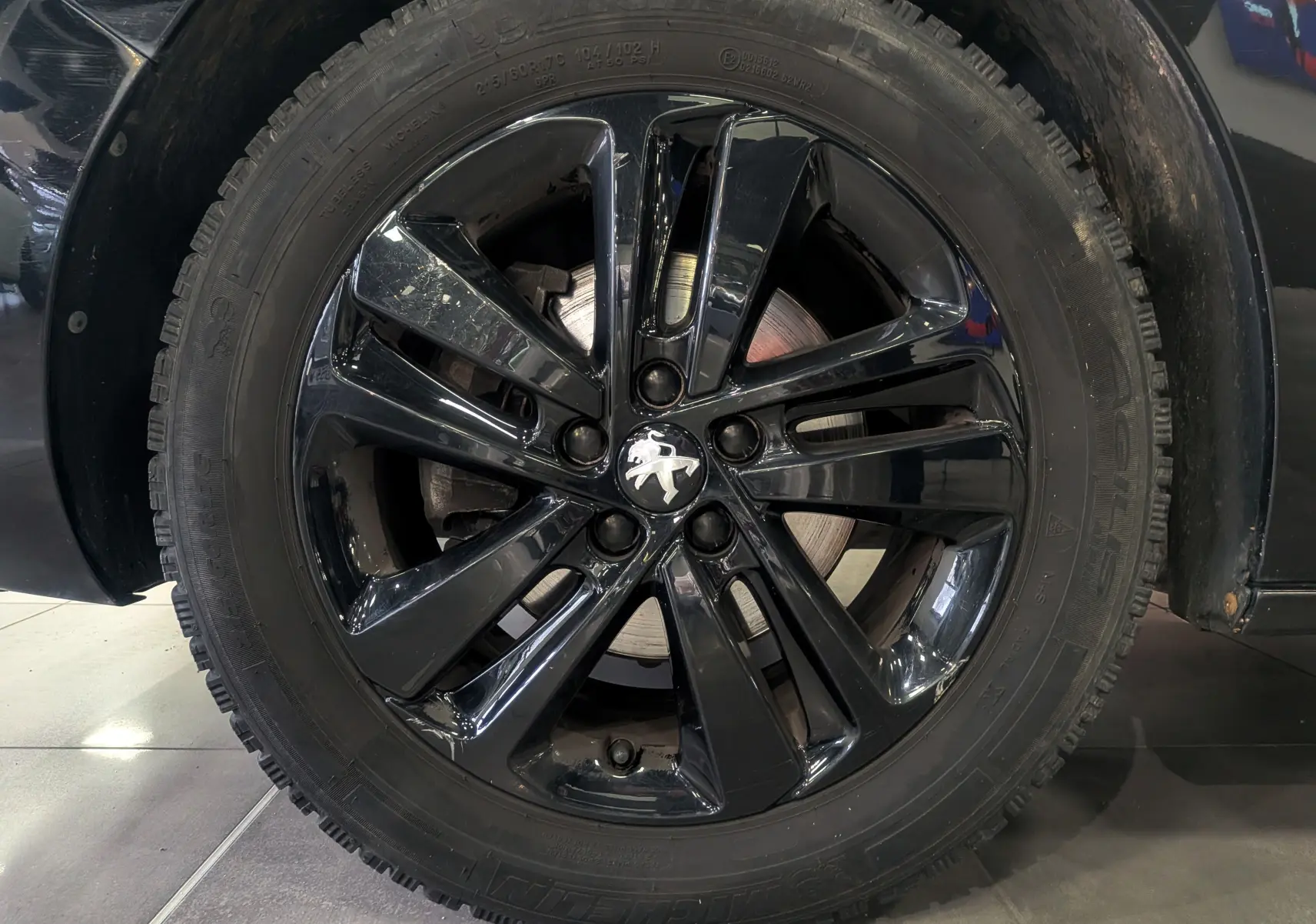 Gros plan sur la jante noire brillante du Peugeot Expert Fourgon noir Perla, mettant en valeur le logo lion au centre.