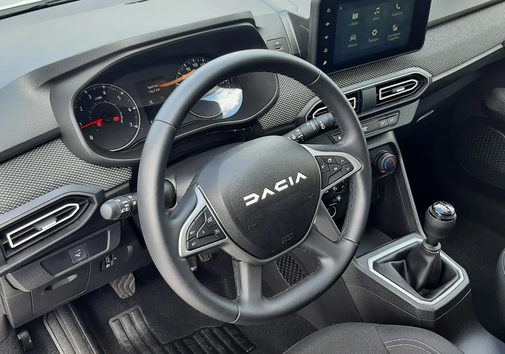 Vue intérieure côté conducteur du tableau de bord et volant DACIA Sandero 2024, finition noire avec boîte manuelle.