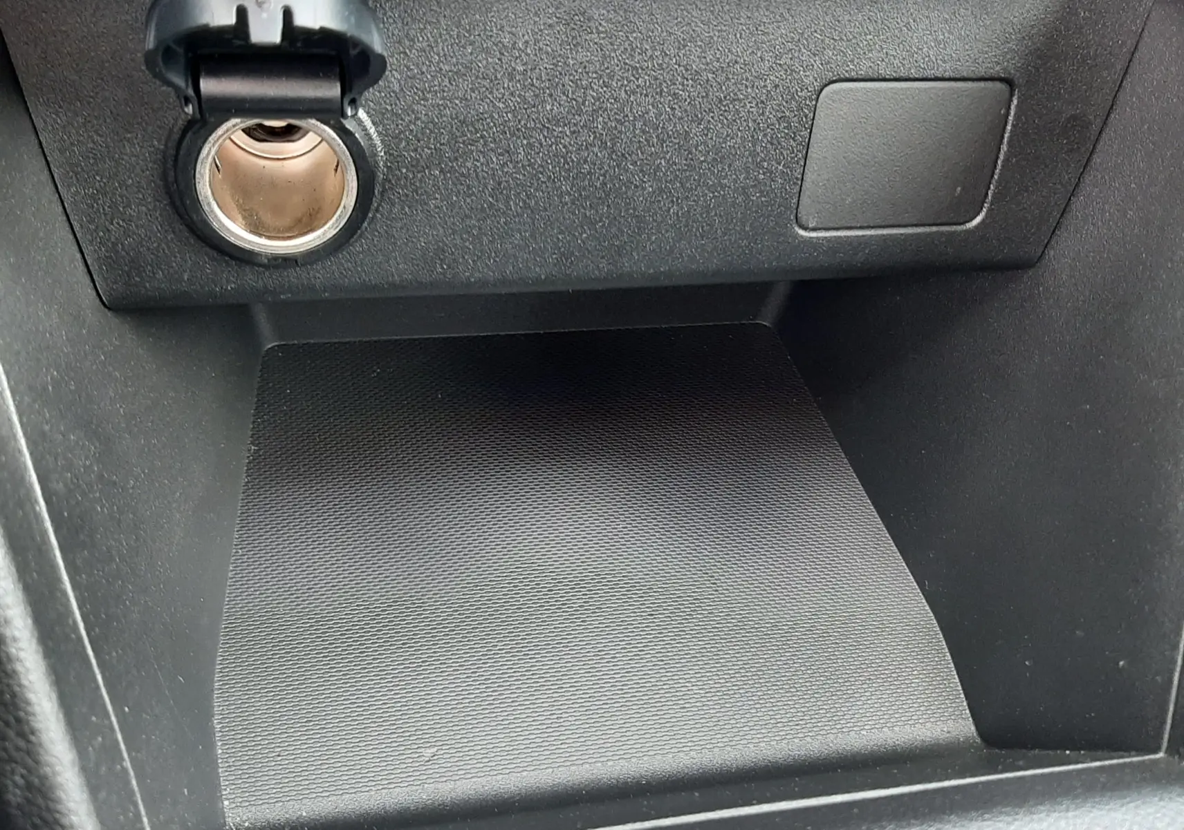 Gros plan sur la prise 12V et le rangement noir texturé du tableau de bord de la Dacia Sandero 2024.