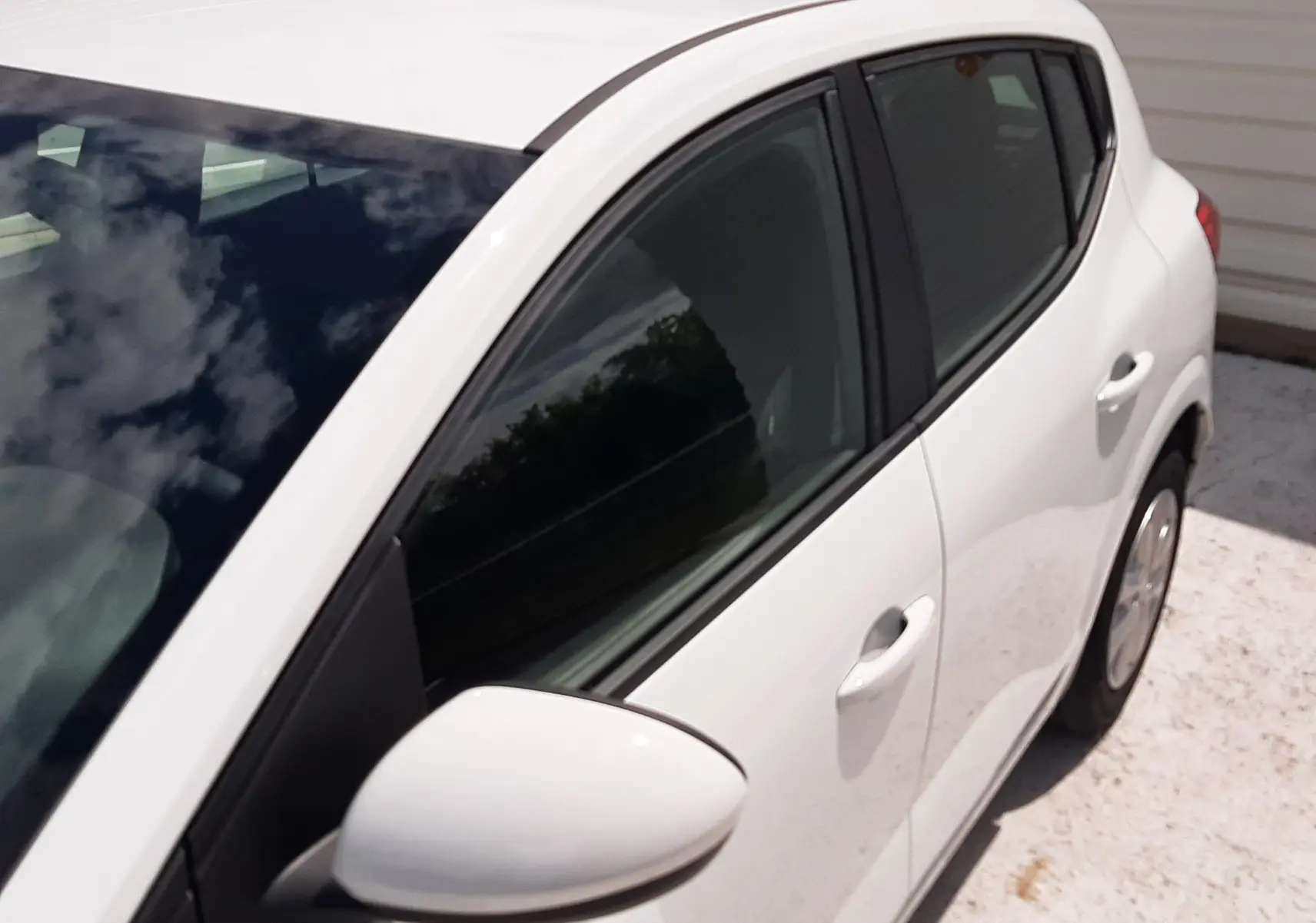Vue en plongée du côté gauche arrière d'une Dacia Sandero blanc glacier, mettant en valeur les vitres teintées et la poignée de porte.